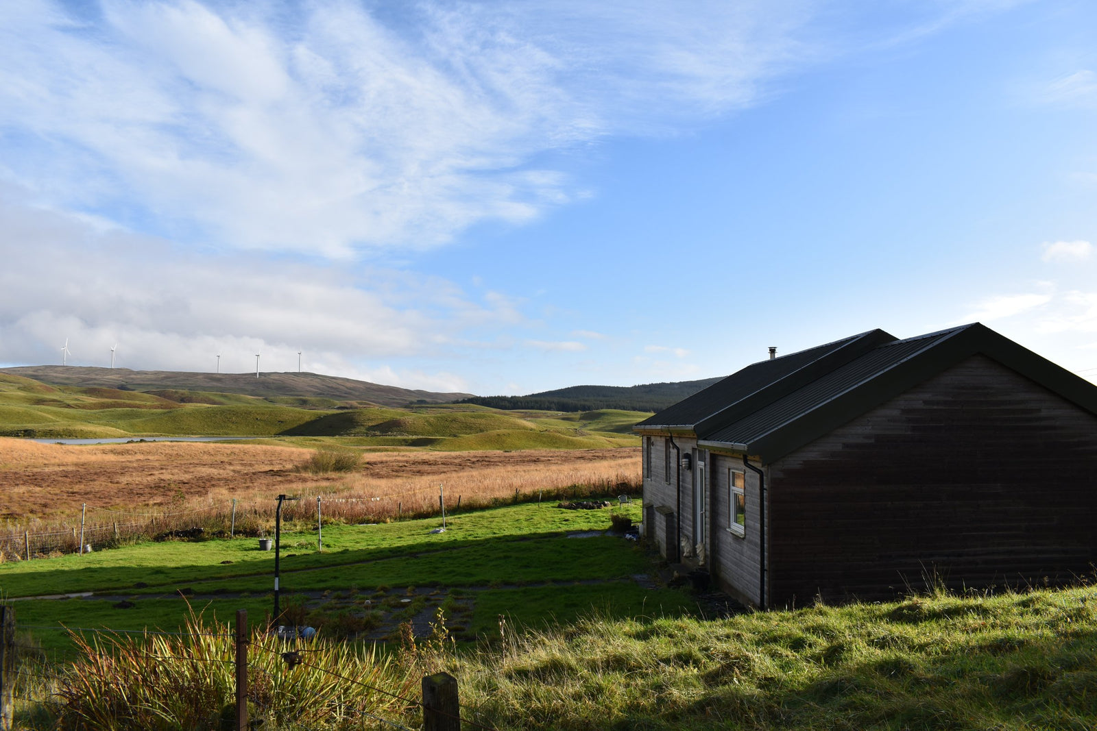 Off-grid house on moorland at Loch Walton with a wind farm on the hills behind